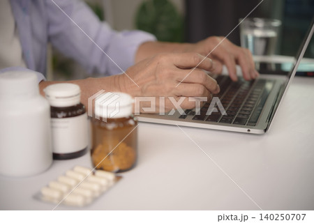 Senior woman using laptop computer at home with medicine bottles and pills on table. Concept of online pharmacy, ordering prescription drugs, and telemedicine for elderly healthcare. Senior woman using laptop computer at home with medicine bottles and pills on table. Concept of online pharmacy, ordering prescription drugs, and telemedicine for elderly healthcare. 140250707