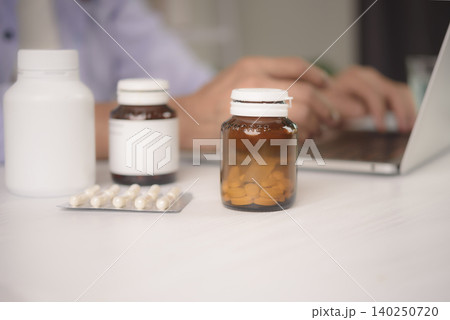 Close up medicine bottles, vitamin supplement and blister pack on table. Senior woman using laptop for ordering prescription pharmacy online or consulting doctor via telemedicine in blurred Close up medicine bottles, vitamin supplement and blister pack on table. Senior woman using laptop for ordering prescription pharmacy online or consulting doctor via telemedicine in blurred 140250720