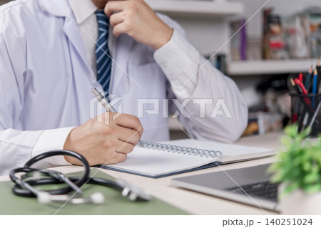 Doctor, healthcare Physician writes notebook at clinic office hospital document patient record, plan diagnosis and treatment, stethoscope and laptop, accurate medical paperwork and care quality. 140251024