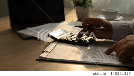 Person using a calculator while reviewing financial documents beside a laptop on a desk, supporting accounting calculation, recordkeeping, budgeting, reporting, and document management workflow. Person using a calculator while reviewing financial documents beside a laptop on a desk, supporting accounting calculation, recordkeeping, budgeting, reporting, and document management workflow. 140251317