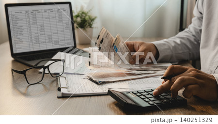Person reviewing personal income tax forms and receipts while using calculator beside laptop for expense tracking, accounting analysis, tax filing, and financial reporting workflow. 140251329