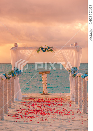 Rose petals scattered along the aisle toward a sunset wedding arch. Vertical view of a romantic ceremony glowing at dusk. Intimate beachfront altar framed by warm golden light. Dreamy destination 140252198