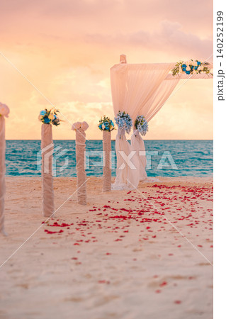 Romantic beach wedding altar draped in white fabric with rose petals lining the sand. Vertical destination ceremony facing the calm tropical sea. Dreamy seaside celebration awaiting the perfect vows.  140252199