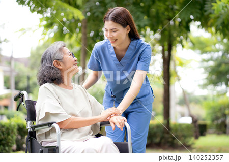 Young caucasian nurse comforting with patient while sitting on wheelchair in outdoor park. 140252357