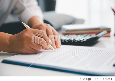 Professional hand signing document on clipboard with calculator in soft focus, showing contract review, paperwork approval, finance planning, legal workflow, and office productivity. Professional hand signing document on clipboard with calculator in soft focus, showing contract review, paperwork approval, finance planning, legal workflow, and office productivity. 140257064