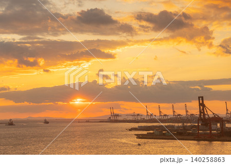 Golden sunset over a busy industrial port with cargo ships and cranes Golden sunset over a busy industrial port with cargo ships and cranes 140258863