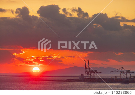 Vibrant sunset over the ocean with industrial cranes and distant mountains 140258866