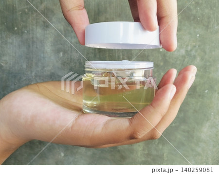 Hand Holding Transparent Cosmetic Gel Jar on Concrete Wall Background Hand Holding Transparent Cosmetic Gel Jar on Concrete Wall Background 140259081