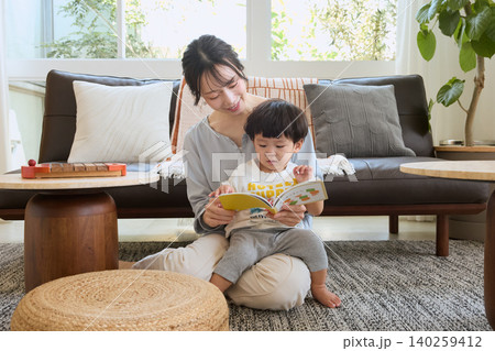 リビングで子どもに絵本の読み聞かせをする若い母親 リビングで子どもに絵本の読み聞かせをする若い母親 140259412