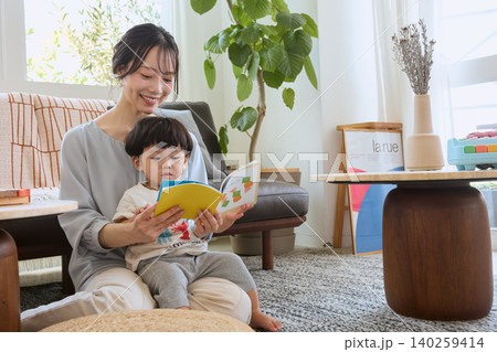 リビングで子どもに絵本の読み聞かせをする笑顔の若い母親 140259414