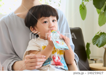母親の膝の上でオーガニックベビーフードを食べる幼児 母親の膝の上でオーガニックベビーフードを食べる幼児 140259427