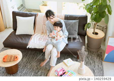 リビングのソファで子どもにおやつを食べさせる母親 リビングのソファで子どもにおやつを食べさせる母親 140259429