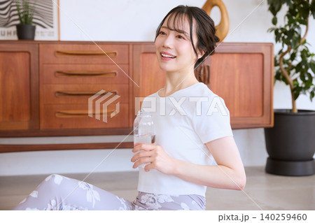 自宅でヨガの休憩中に水を飲む笑顔の若い女性 自宅でヨガの休憩中に水を飲む笑顔の若い女性 140259460