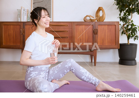 自宅でヨガの休憩中に水を飲む笑顔の女性 自宅でヨガの休憩中に水を飲む笑顔の女性 140259461