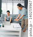 Asian parent bringing a sandwich to a young woman using a laptop on a sofa at home, showing family support, remote work, study break, caregiving, nutrition, and caring domestic lifestyle. 140259967