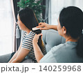 Asian parent gently brushing a young woman's long hair on a sofa at home, showing family bonding, hair care, caregiving, beauty routine, tenderness, support, comfort, and daily love. 140259968