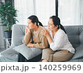 Asian parent comforting a sad young woman on a sofa at home, showing emotional support, family care, empathy, anxiety relief, counseling, trust, and mental wellness in a bright living room. 140259969