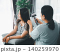 Asian parent drying a young woman's long hair with a hair dryer on a sofa at home, showing family care, beauty routine, grooming, support, bonding, everyday care, and domestic lifestyle. 140259970