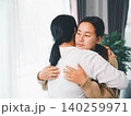 Asian parent hugging a young woman at home, showing family comfort, emotional support, empathy, reconciliation, mental wellness, caregiving, trust, and a healing relationship in a bright living room. 140259971