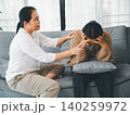 Asian parent supporting a distressed young woman holding her head on a sofa at home, showing family empathy, crisis support, mental wellness, caregiving, comfort, and trusted help. 140259972
