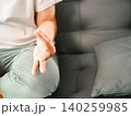 Close-up of an Asian woman practicing a calming hand gesture while sitting on a sofa at home, showing mindfulness, meditation, relaxation, breathing, wellness, and peaceful self care. 140259985