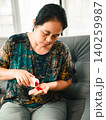 Asian woman pouring red pills from a bottle into her hand while sitting on a sofa, representing medication routine, healthcare, treatment, wellness, home care, and personal health. 140259987