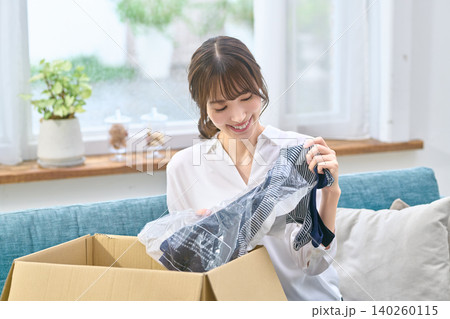 段ボールから届いた洋服を取り出す笑顔の女性 段ボールから届いた洋服を取り出す笑顔の女性 140260115