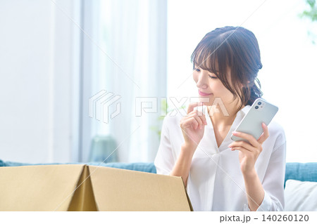 段ボールの横でスマホを見て微笑む女性 段ボールの横でスマホを見て微笑む女性 140260120