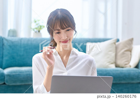 自宅でノートパソコンを見ながらペンを持つ若い女性 自宅でノートパソコンを見ながらペンを持つ若い女性 140260176