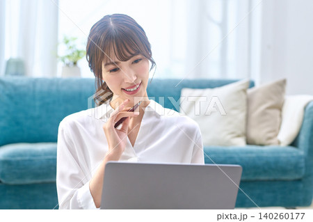 自宅でパソコンを見ながら考える笑顔の若い女性 自宅でパソコンを見ながら考える笑顔の若い女性 140260177
