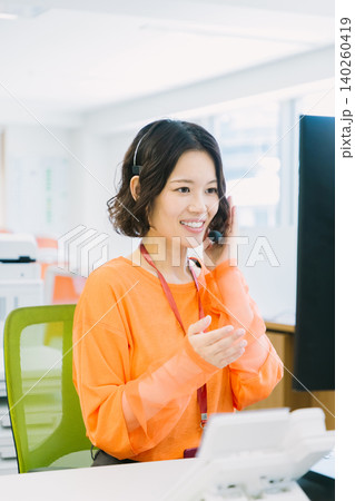 オフィスでヘッドセットをつけて応対する女性オペレーター 140260419