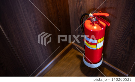 Red tank of fire extinguisher placed at the corner of wooden corridor in public building 140260525