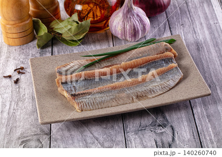 Pickled herring fillets on ceramic plate with spices and garlic on wooden table 140260740