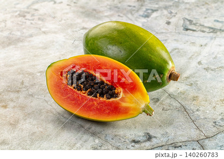 Fresh papaya fruit whole and halved showing orange flesh and black seeds on stone surface Fresh papaya fruit whole and halved showing orange flesh and black seeds on stone surface 140260783