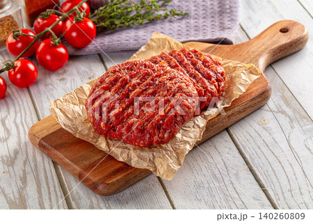 raw beef burger patties on wooden board with tomatoes and thyme raw beef burger patties on wooden board with tomatoes and thyme 140260809
