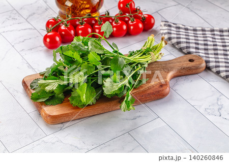 Fresh green cilantro bunch on wooden cutting board with cherry tomatoes and oil bottle Fresh green cilantro bunch on wooden cutting board with cherry tomatoes and oil bottle 140260846