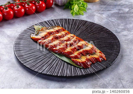 Grilled eel fillet on black plate with cherry tomatoes 140260856