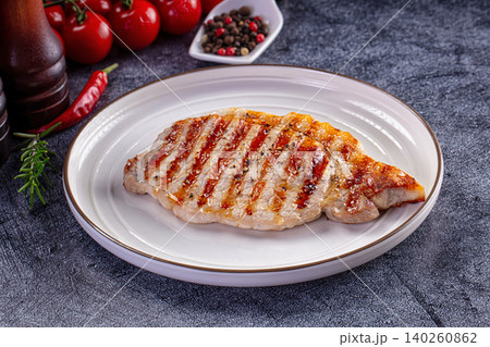 Grilled pork steak on white plate with fresh vegetables and spices 140260862