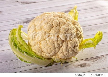 A whole fresh cauliflower with green leaves on a light rustic wooden table 140260949