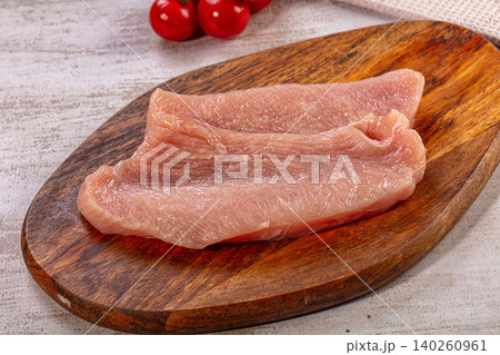Raw chicken breast fillet on wooden cutting board with cherry tomatoes in background Raw chicken breast fillet on wooden cutting board with cherry tomatoes in background 140260961