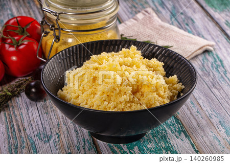 Couscous in black bowl with tomatoes and jar on rustic wooden table 140260985