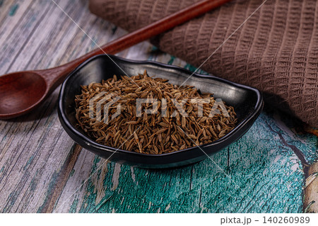 Dried cumin seeds in black bowl with wooden spoon Dried cumin seeds in black bowl with wooden spoon 140260989