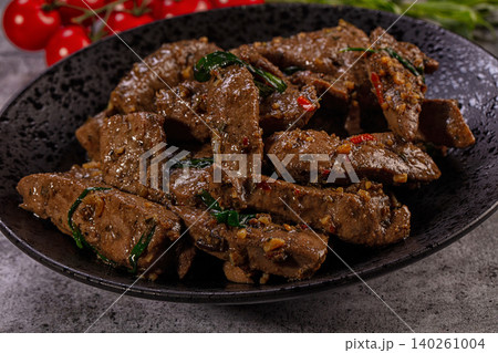 Spicy fried beef liver with basil and chili pepper in black bowl, close-up Spicy fried beef liver with basil and chili pepper in black bowl, close-up 140261004