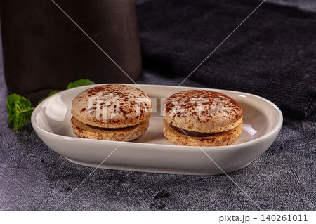 Two chocolate macarons dusted with cocoa powder on a white ceramic plate Two chocolate macarons dusted with cocoa powder on a white ceramic plate 140261011