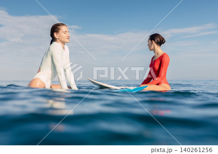 Two girl surfers sitting on surfboards in calm ocean waiting for surfing waves Two girl surfers sitting on surfboards in calm ocean waiting for surfing waves 140261256
