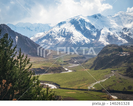 Snow-capped peaks rise above lush green valleys, Kazbegi region. Snow-capped peaks rise above lush green valleys, Kazbegi region. 140261328