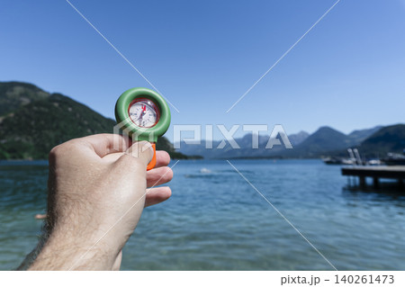 Hand holding a portable compass over a lake with mountains in the background, suitable for travel use and practical field tasks Hand holding a portable compass over a lake with mountains in the background, suitable for travel use and practical field tasks 140261473