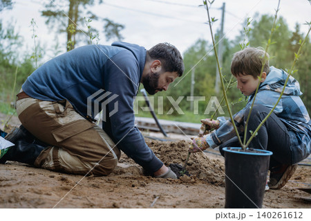 A man and caucasian boy planting a dogwood shrub together on their countryside property A man and caucasian boy planting a dogwood shrub together on their countryside property 140261612