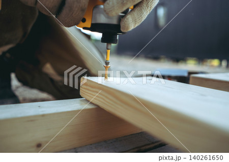 Close-up of a man hands driving a screw with a cordless drill while constructing a tall raised garden bed on a countryside property Close-up of a man hands driving a screw with a cordless drill while constructing a tall raised garden bed on a countryside property 140261650