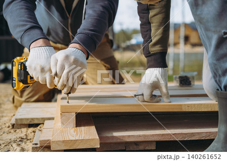 Close-up of a man hands driving a screw with a cordless drill while constructing a tall raised garden bed on a countryside property Close-up of a man hands driving a screw with a cordless drill while constructing a tall raised garden bed on a countryside property 140261652